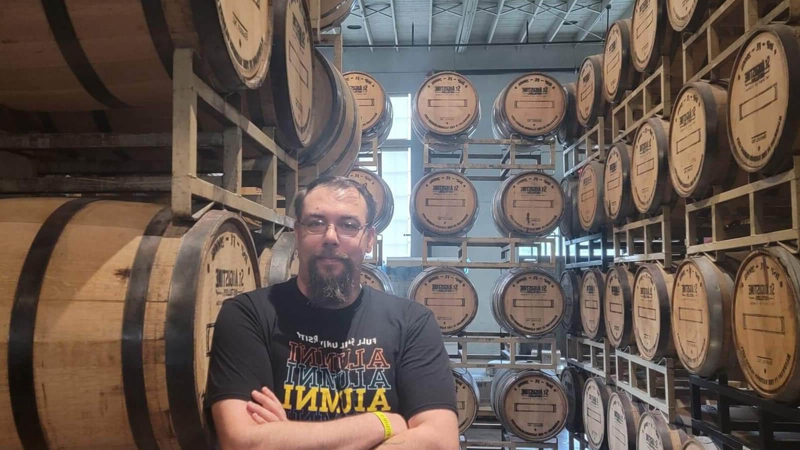 Daniel Vanallen sits in a chair at St. Augustine Distillery Co. He is smiling and wearing a Full Sail Alumni shirt.