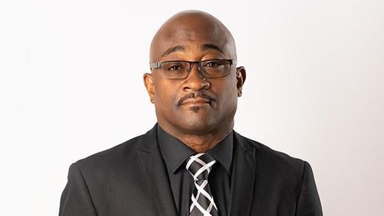 A headshot of Christopher Rapley wearing glasses and an all-black suit with a black-and-white tie and pocket square.