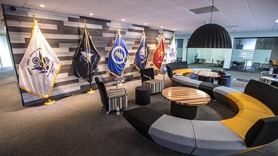 An image of 满帆’s 军事 Student Success center shows a large couch, 小型会议室, and flags representing each branch of the US Armed Services.