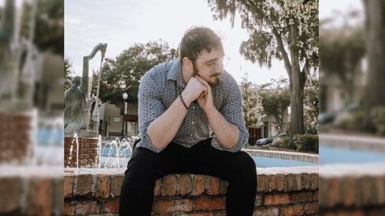 长得短的人, 黑暗, curly hair in a blue button down shirt and wireframe glasses looking to the side while sitting in front of a fountain.