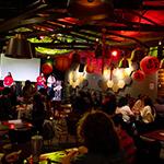 A group gathered at 满帆's Treehouse, guests sitting down 和 the hosts on stage. The room is dimly lit 和 decorated with red paper lanterns for the Lunar New Year.